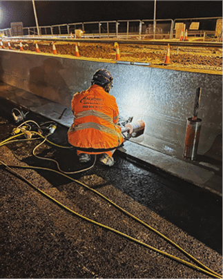 Ralkore operator core drilling through a concrete road barrier at night